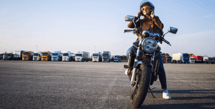 Jovem mulher sorridente a andar de moto numa rua da cidade.
