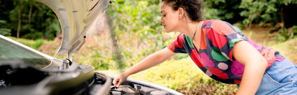 Mulher jovem analisa a bateria do carro.