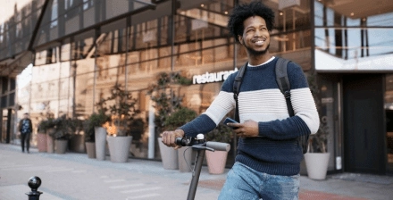 Jovem atravessa o passeio com uma trotinete elétrica na mão.