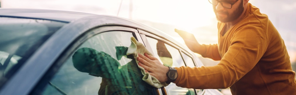 Rapaz a fazer limpeza automóvel ao exterior do seu carro.
