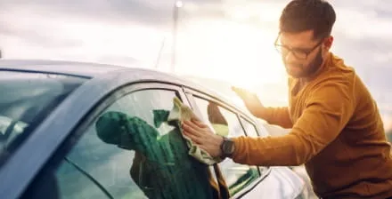 Rapaz a fazer limpeza automóvel ao exterior do seu carro.