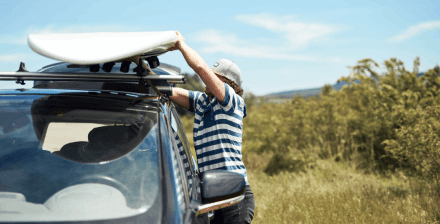 Homem jovem a colocar carga nas barras tejadilho do seu carro.